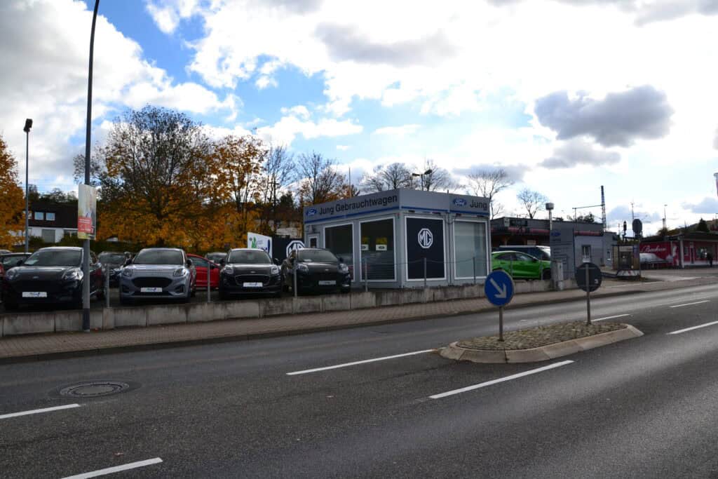 Autohändler mit mehreren schwarzen Fahrzeugen, wolkiger Himmel, herbstliche Bäume im Hintergrund.